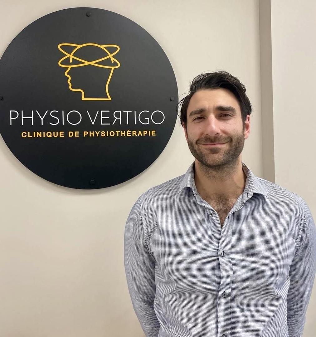 Frédéric Michaud standing beside the round gold Physio Vertigo clinic sign